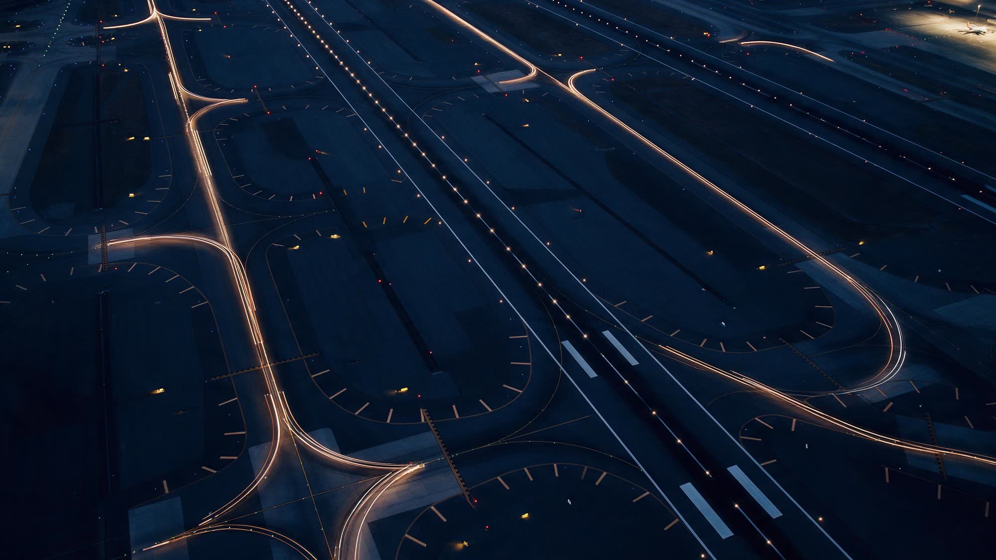 An airfield at night from above, light trails tracing the taxiways