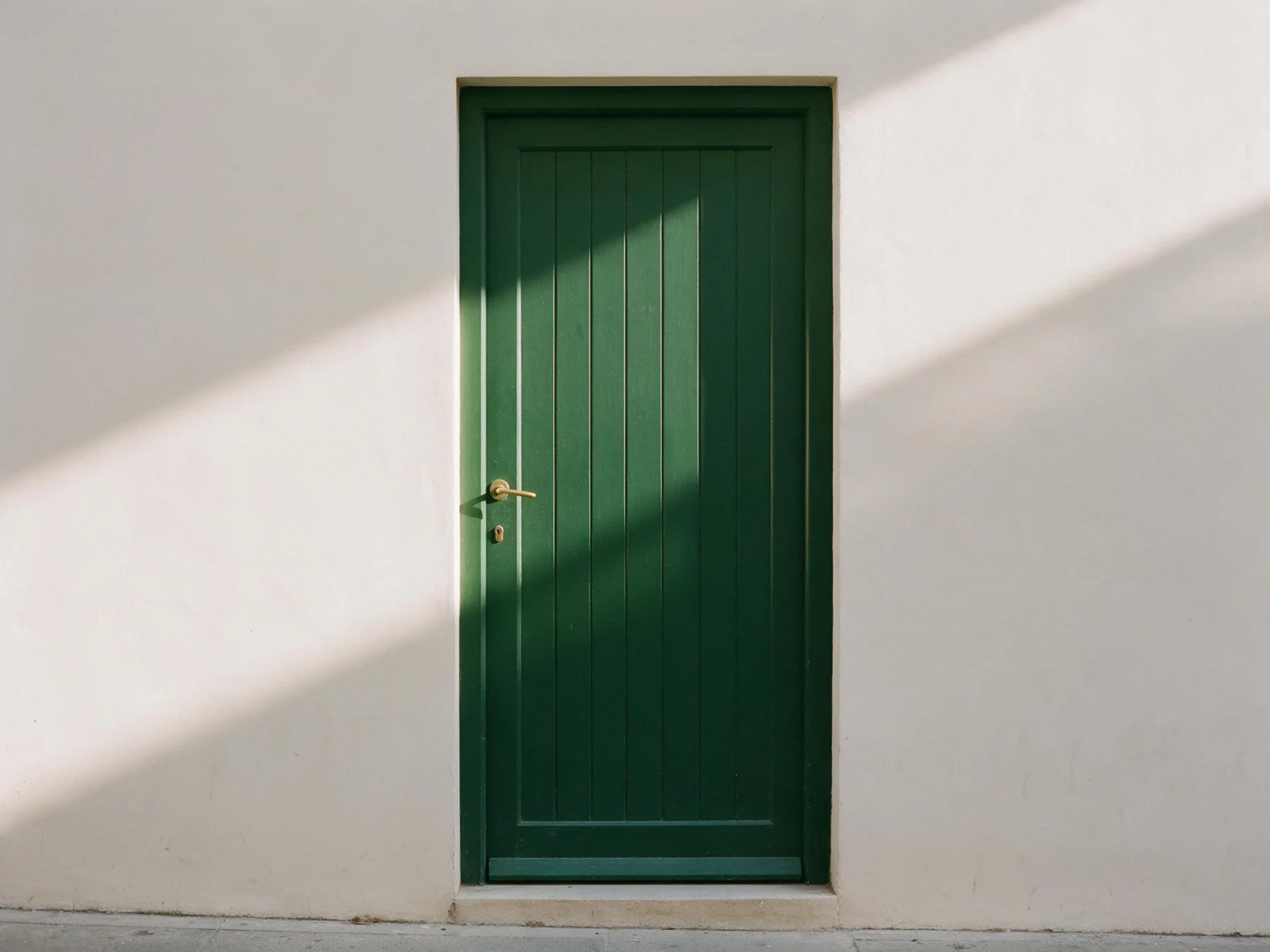 A single green wooden door in a sunlit plaster wall.